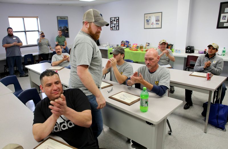 John Burk (center) receives applause Friday during a graduation at Northwest Technical Institute’s Business and Industry Training Center in Springdale. Eight completed a month-long course to become apprentice maintenance technicians.