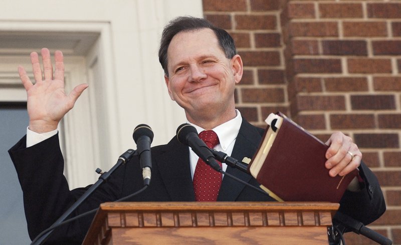 The Associated Press MOORE: In this Thursday, Nov. 6, 2003, photo, former Alabama Chief Justice Roy Moore holds his Bible as he acknowledges the applause during his speech at the Barrow County Court House in Winder, Ga. Moore drew rounds of applause as he spoke in support of the framed Ten Commandments in the courthouse breezeway.