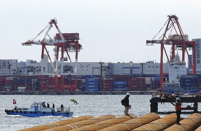 At a seaside construction site in March, workers stand near the pier of a container terminal in Tokyo. Japan reported Monday that its imports rose almost 19 percent from the same month a year earlier while exports were up 14 percent. The country’s trade surplus dropped more than 40 percent.