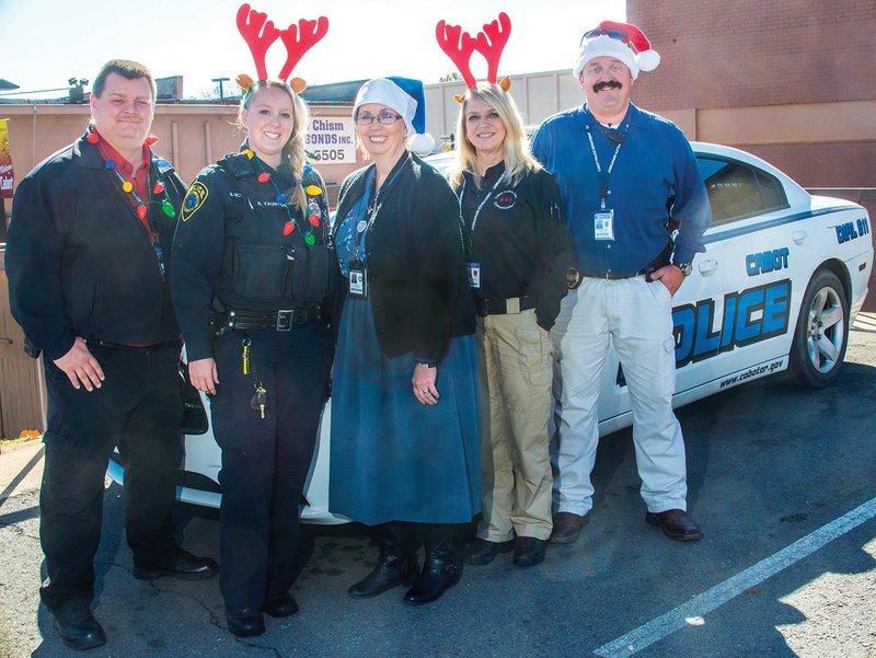Cabot Police Department Capt. Brent Lucas, from left, resource officer Brittany Tauton, chaplain Tina Frost, dispatch lead Teresa Young and Lt. Robby Gibson pose in front of a police car. The Cabot Officers Playing Santa Toy Patrol, or C.O.P.S. Toy Patrol, is centered around providing Christmas gifts to children in need.