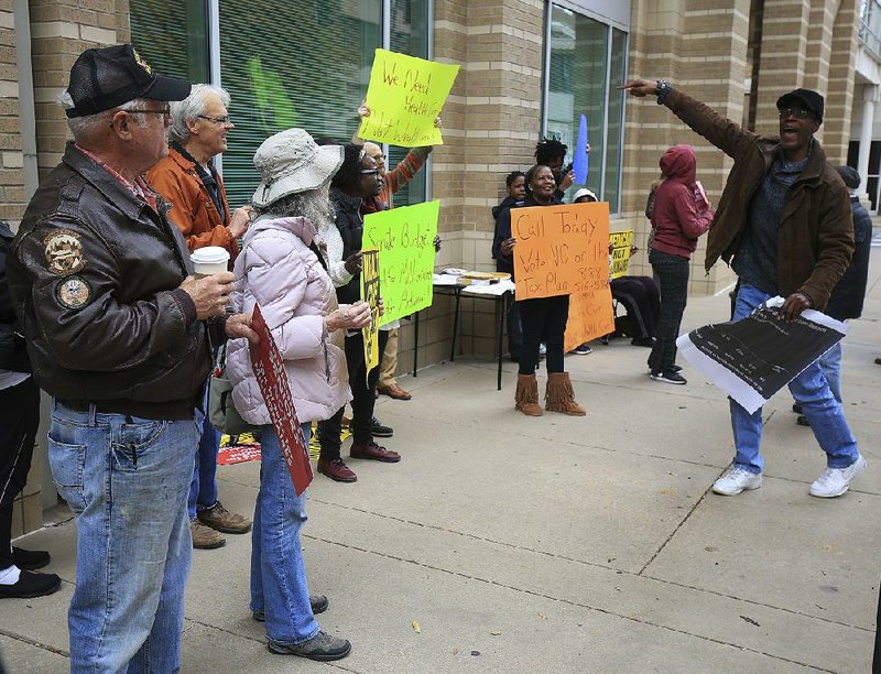 Tony Orr (right) of Little Rock leads a chant Tuesday as a group of people rally near the state Department of Human Services offices on Main Street in Little Rock to oppose a GOP-proposed tax overhaul in Congress. 