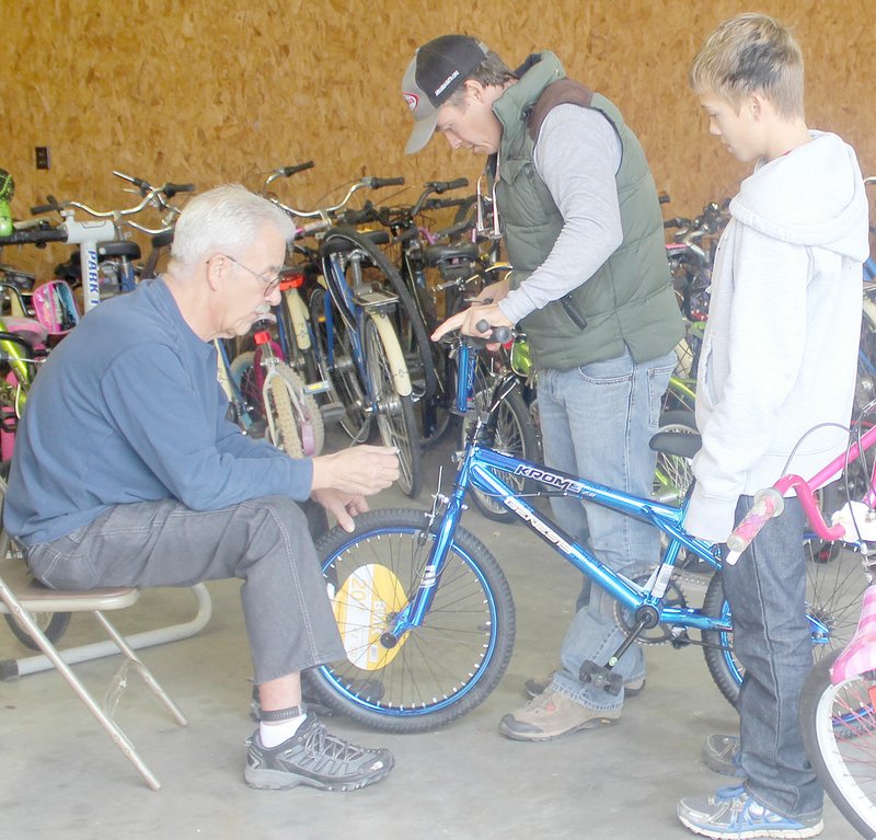 Keith Bryant/The Weekly Vista Bella Vista resident and Pedal it Forward volunteer John Krafft (left) shows first-time volunteers Sterling Minick and his son Oskar Minick, 13, how to adjust cable tension on brake levers.
