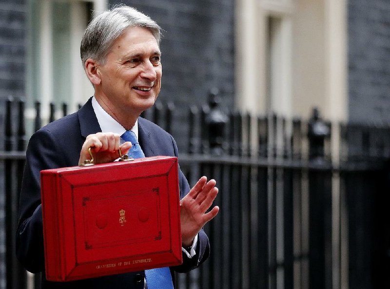 Britain's Chancellor of the Exchequer Philip Hammond waves and poses for the media as he holds up the traditional red dispatch box, outside his official residence 11 Downing Street, before delivering his annual budget speech to Parliament, in London, Wednesday, Nov. 22, 2017. 