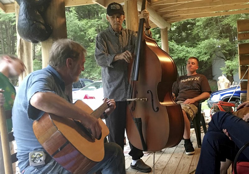 AP/MARGIE MASON In this Oct. 12, 2017 photo, Mike Baughman (center) plays the bass Oct. 12 with Sam Gibson (left) on guitar while Ryan Baughman looks on at a cabin in Herald, W.Va. Mike Baughman is fighting a rare bile duct cancer he believes is a result of ingesting a parasite inside raw fish while serving in the Vietnam War. The U.S. Department of Veterans Affairs has commissioned a study, the first of its kind in the United States, to look into the link between liver flukes and the disease.
