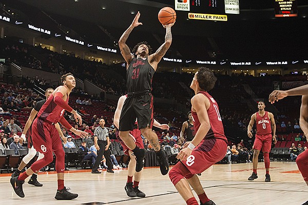 Arkansas guard Anton Beard, center, scores a basket as he is guarded by Oklahoma guard Trae Young, right, and center Jamuni McNeace, left, during the second half of an NCAA college basketball game at the Phil Knight Invitational tournament, in Portland, Ore., Thursday Nov. 23, 2017. (AP Photo/Troy Wayrynen)

