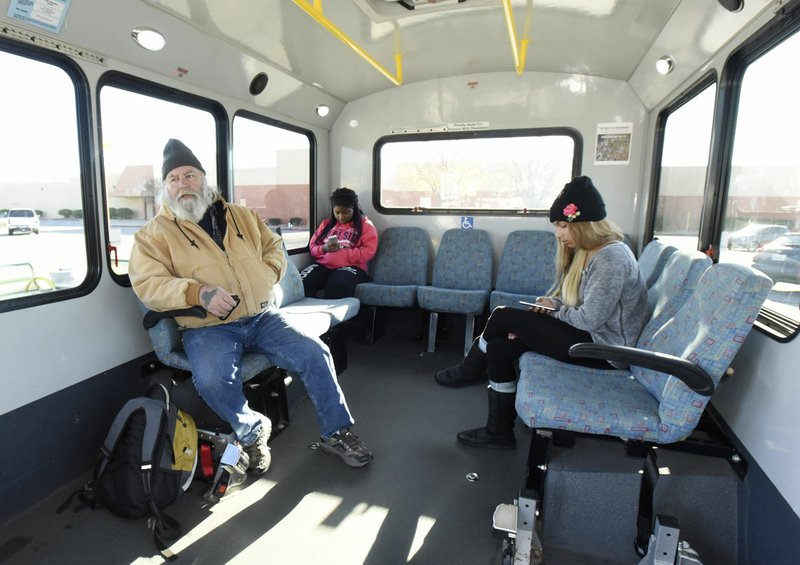 Justin Cunningham (left) of Bentonville, a regular Ozark Regional Transit passenger, waits Wednesday for a bus to depart from a stop in Rogers. Cunningham said the bus service is excellent.