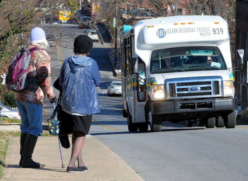 Passengers wait Wednesday to board an Ozark Regional Transit bus near the intersection of North School Avenue and West Center Street in Fayetteville.