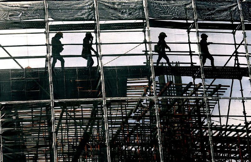 Workers cross a section of scaffolding at a construction site in Bangkok on Tuesday. The Organization for Economic Cooperation and Development on Tuesday predicted economic growth worldwide next year but warned investors that asset prices have gotten too high for a global economy and a market downturn could put the expansion at risk. 