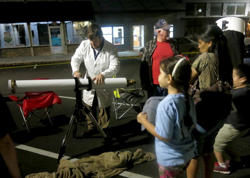 Photo by Susan Holland Van Masterson, events coordinator for NWA Space in Fayetteville, was on hand at the Gravette Public Library's star party Friday, Nov. 17, to explain the workings of the telescopes his group provided. Here he prepares to show Al Blair, Maria Pinto and her children Dina Teed and Paul Teed (partially hidden) how to use the finder scope he has set up. Dina holds one of the evening star maps provided to star party guests.