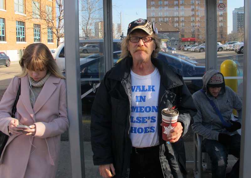 In this Nov. 21 photo, former security guard Tim Button poses for a portrait at the bus stop to take a local ride, a recent luxury he at one time could not afford in Hamilton, Ontario, Canada. Button says he has been unable to work because of a fall from a roof and the financial boost from the province's basic income program has enabled him to make plans to visit distant family for Christmas for the first time in years. (AP Photo/Rob Gillies)