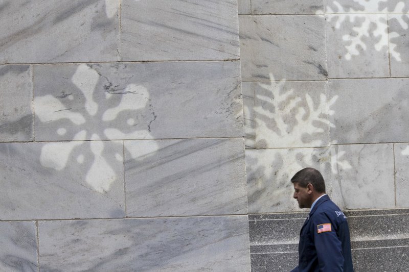 In this Thursday, Nov. 30, 2017, photo, a broker walks past snowflake lighting decorating the facade of the New York Stock Exchange. U.S. stocks veered sharply lower Friday, Dec. 1, as investors worried that former national security adviser Michael Flynn's guilty plea to lying to the FBI could spell trouble for the White House and its legislative agenda, including a tax overhaul currently under debate in Congress. (AP Photo/Mary Altaffer)