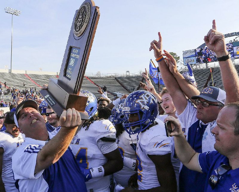 Coach Jamie Mitchell (left) holds the Class 7A state championship trophy while celebrating with his team Saturday after the Charging Wildcats defeated the Bentonville Tigers 44-37 at War Memorial Stadium.