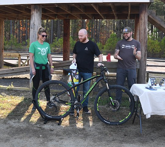 The Sentinel-Record/Mara Kuhn - Heath Netzley of Little Rock, center, accepts prizes for Darren Houston of Little Rock, as Drea Poteete, owner of Spa City Cycling, left, and Brian Marcus, with Local Arkansas, look on at Cedar Glades Park on Saturday, Dec. 2, 2017. Houston won the Natural Arkansas November photography contest on Instagram.