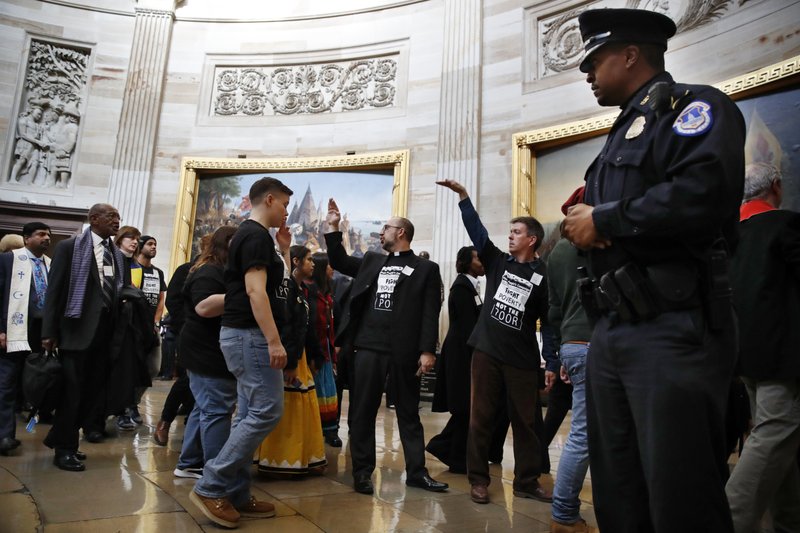 The Associated Press CIVIL DISOBEDIENCE: With shirts saying "fight poverty not the poor," people with the "Poor People's Campaign" gesture the group to remain quiet as the group leaves the Capitol Rotunda after praying in an act of civil disobedience in protest of the GOP tax overhaul, Monday, Dec. 4 on Capitol Hill in Washington.