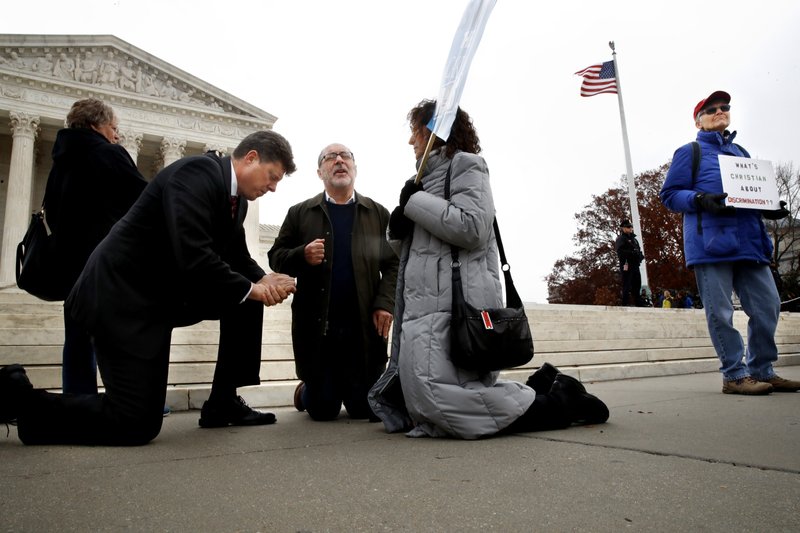 The Associated Press PRAYING AND PROTESTING: Rev. Brad Wells, left, Rev. Patrick Mahoney, and Paula Oas, kneel in prayer in front of the Supreme Court, as a counter-protester holds a sign that says "What's Christian About Discrimination," while the court hears the 'Masterpiece Cakeshop v. Colorado Civil Rights Commission' case, Tuesday in Washington.