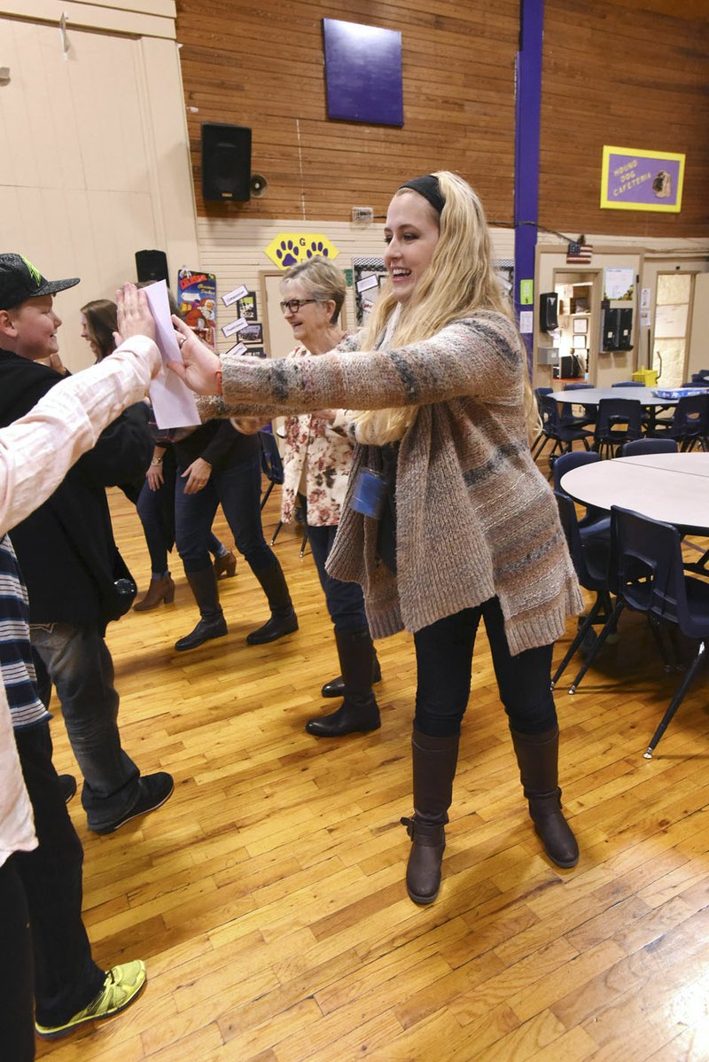 Kayla Wiles (right), music teacher at Garfield Elementary School, sings and dances Thursday with students during the school song after she received a $500 grant from the Rogers Public School Foundation. Foundation members, including Diana Kolman (second from right) delivered grant checks to teachers at several School District schools on Thursday. Wiles plans to purchase musical instruments with her grant.