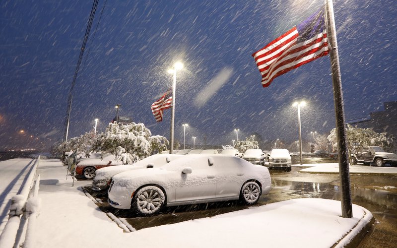 American flags wave as snow falls, blanketing vehicles in a car sales lot, Friday, Dec. 8, 2017, in Jackson, Miss. The forecast called for a wintry mix of precipitation across several Deep South states.