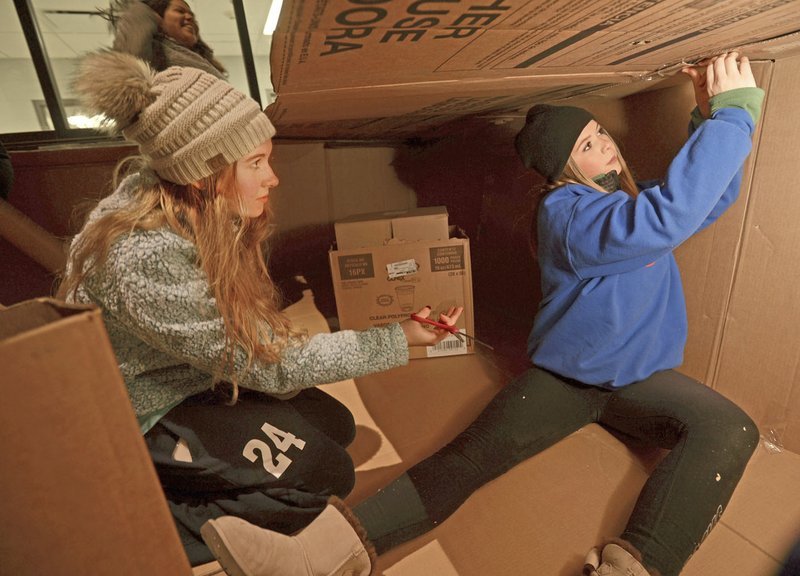 NWA Democrat-Gazette/ANDY SHUPE Whitney Waitsman (left) and Kennedy Combs, both sophomore members of Fayetteville High School's Student Council, put together a cardboard shelter Thursday evening during the annual Homeless Vigil. Council members spent the night outside in makeshift shelters outside the school to raise money for the district's Families in Transition program.