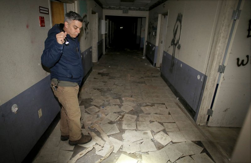 Palmer illuminates floor tiles Thursday containing asbestos in the old City Hospital. Asbestos will be pulled out of the ceiling and scraped from the floor tile. The material will go into bags capable of hauling it and placed into a lined trash bin.