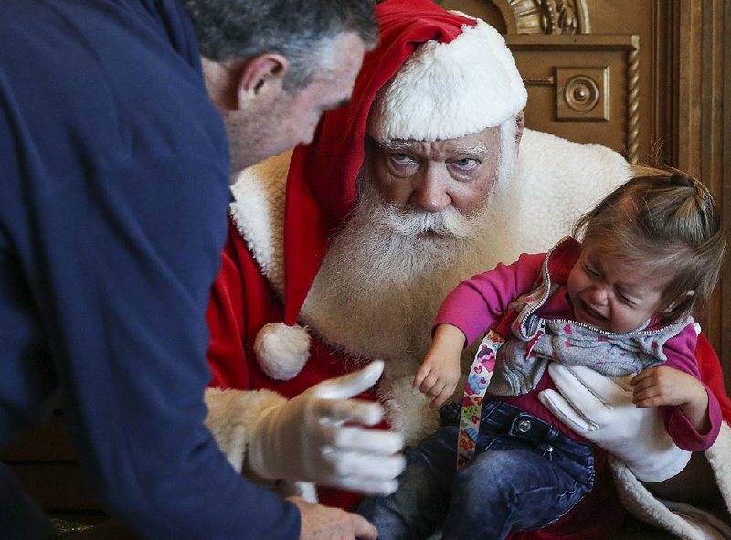 Adrian Hawkins of Little Rock tries to get his granddaughter, 18-month-old Elliott Allie, to settle down for Santa Claus, played by Carroll Dunn, during the Santa at the Center event Saturday at the Clinton Presidential Center in Little Rock. Elliott was visiting Little Rock with her parents from Brentwood, Tenn.