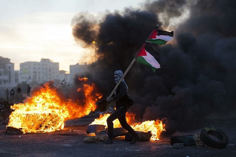 A demonstrator carries a Palestinian flag Saturday during clashes with Israeli troops in the West Bank city of Ramallah, one of several “day of rage” protests in the West Bank and Gaza.