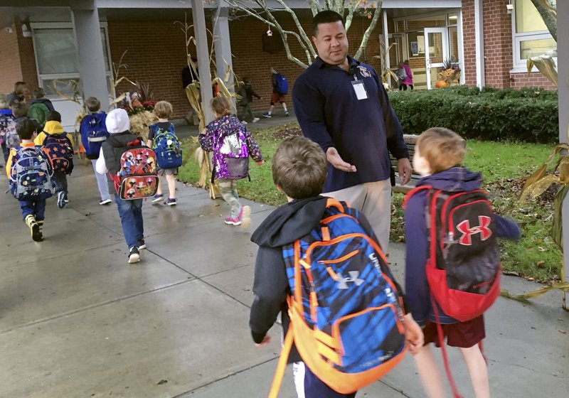 In this Nov. 6, 2017 photo, campus monitor Hector Garcia greets students as they got off the bus at the start of the school day at West Elementary School in New Canaan, Conn. Garcia and the district's other campus monitors -- all former police or corrections officers -- were among a wave of security officers hired in the aftermath of the deadly school shooting in nearby Newtown on Dec. 14, 2012. 