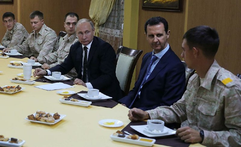 Russian President Vladimir Putin, center left, and Syrian President Bashar Assad, 2nd right, meet with military personnel at the Hemeimeem air base in Syria, on Monday, Dec. 11, 2017. Declaring a victory in Syria, Putin on Monday visited a Russian military air base in the country and announced a partial pullout of Russian forces from the Mideast nation. 