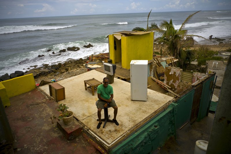 This Oct. 5, 2017 file photo shows Roberto Figueroa Caballero sitting on a small table in his home that was destroyed by Hurricane Maria in La Perla neighborhood on the coast of San Juan, Puerto Rico.