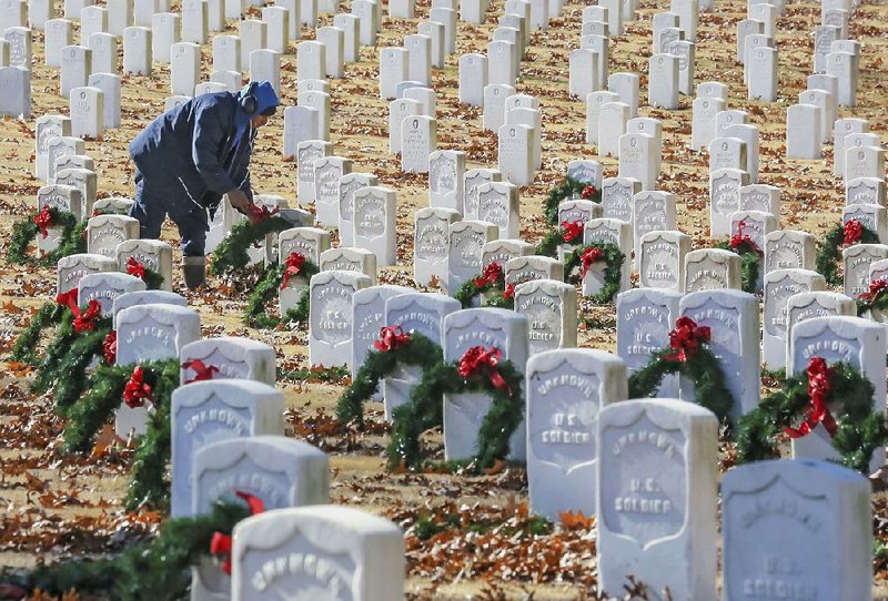 Jerron Devose, an employee of Worrell Contractors, places Christmas wreaths Wednesday on headstones at Little Rock National Cemetery. 