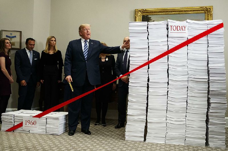 President Donald Trump wields golden scissors Thursday at the White House as he stands between a stack of what he said were pages of government regulations from 1960 and today’s amount.
