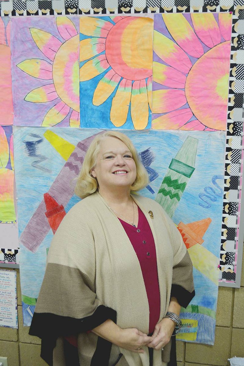 Becky Thornton, who is in her 43rd year as an art teacher in the Conway School District, stands in her Carl Stuart Middle School classroom in front of paintings of flowers, including the one she did, in the upper right-hand corner. Thornton received the Judges Recognition Award from the Arkansas Arts Council in its 2018 Governor’s Arts Awards program and will be honored in March at a luncheon.