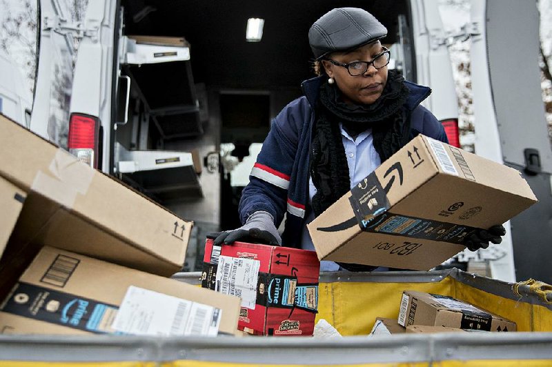 A letter carrier holds Amazon.com packages Tuesday while loading a vehicle for deliveries at a distribution center in Washington, D.C. 