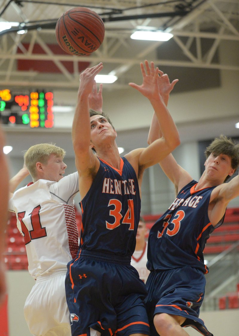 Farmington’s Mason Downs (left) and Rogers Heritage’s Seth Stanley vie for a rebound as Jason Kimball (33) looks Friday during the first half at Cardinal Arena in Farmington.