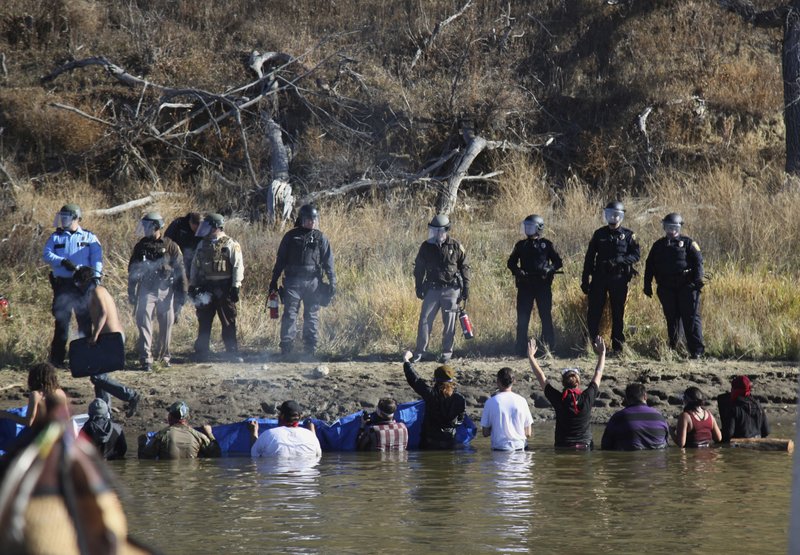In this Nov. 2, 2016 file photo, protesters demonstrating against the expansion of the Dakota Access Pipeline wade in cold creek waters confronting local police as remnants of pepper spray waft over the crowd near Cannon Ball, N.D. North Dakota law enforcement purchased more than $600,000 worth of body armor, tactical equipment and crowd control devices during the height of protests against the Dakota Access oil pipeline, state invoices show.