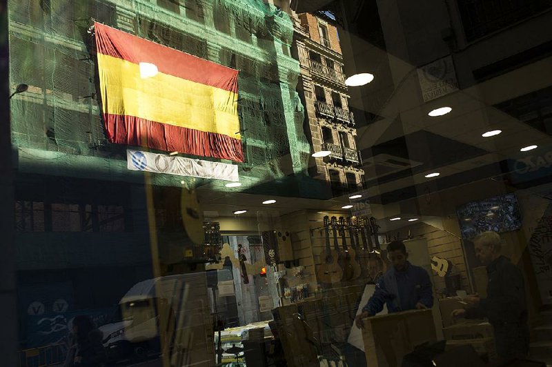A Spanish flag on a Madrid building is re!ected in a shop window Wednesday, a day before Catalan voters return to the polls to elect a new regional government. 
