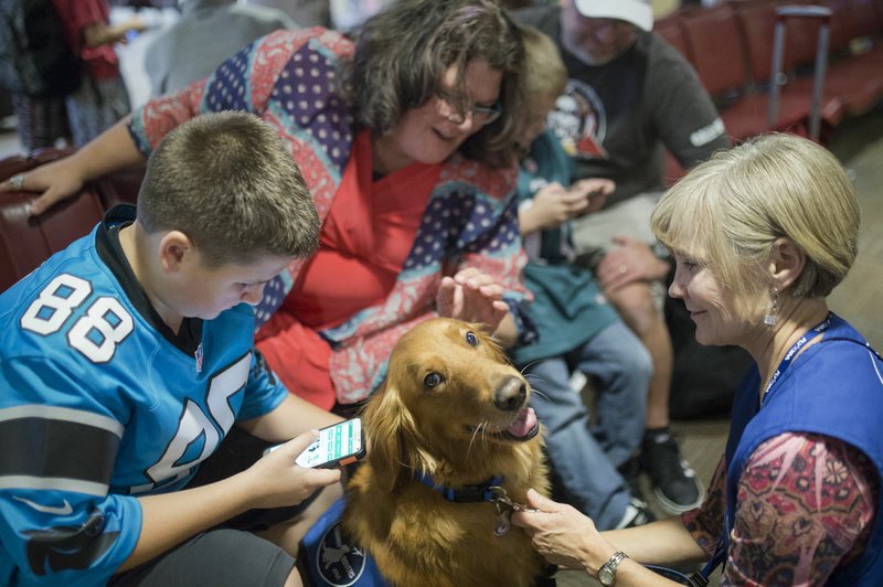 NWA Democrat-Gazette/CHARLIE KAIJO Asher Olsen, Tiffiny Olsen, Sawyer Olsen and Jeff Olsen of Bentonville pet Honey last month as owner Beth Robinson looks on at the Northwest Arkansas Regional Airport in Bentonville. Volunteers bring their trained therapy dogs to XNA ease some stress of traveling and calm passengers.