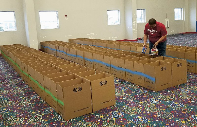 NWA Democrat-Gazette/ASHTON ELEY Bobby Smittle, Kiwanis Club of Bentonville president, adds food to boxes Wednesday for the group's annual Guy Wilkerson Food Basket Giveaway on Saturday in Bentonville.