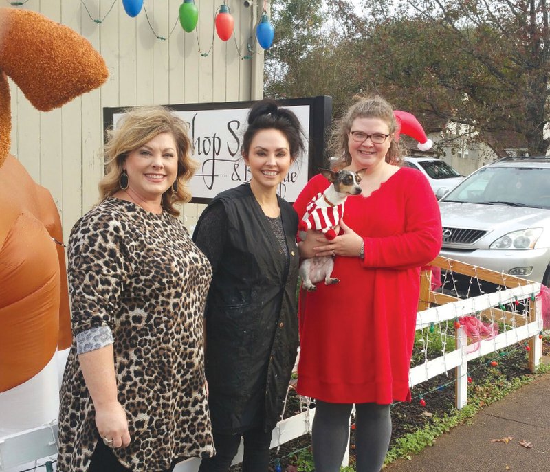 From left, Kris Gravett, chair of the Arkadelphia Downtown Network; Jessica Arnold, owner of the Gossip Shop; and Humane Society of Clark County representative Joy Buck, holding mascot Rex, pose in front of the Gossip Shop in Downtown Arkadelphia. The shop was awarded $1,000 to be donated to the Humane Society as part of the Be the Light event, which took place Nov. 30.