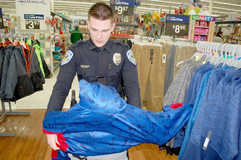 Graham Thomas/Siloam Sunday Siloam Springs Police officer Zachary Ware helps 10-year-old Aaron Engleman try on a hooded sweatshirt during the Cops and Kids event held Wednesday at Walmart Supercenter in Siloam Springs.