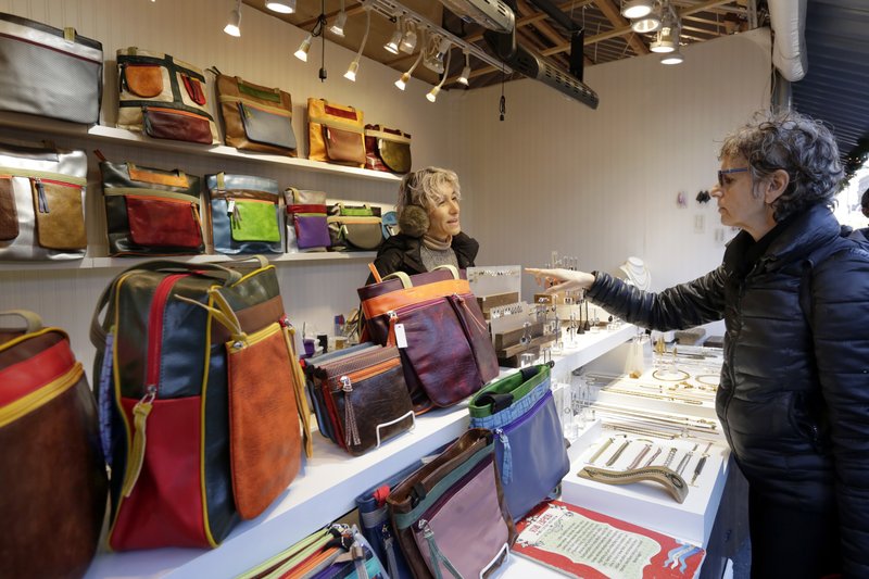 In this Thursday, Dec. 7, 2017, photo, Tanya Carol-Lugones helps a shopper in her booth featuring Viva Zapata bags and Caracruz jewelry, at the Union Square Holiday Market in New York. At the holiday markets that pop up annually, many of the booths are staffed by artisans hoping to make a significant portion of their revenue or to get visibility that will translate into sales other times of the year. (AP Photo/Richard Drew)