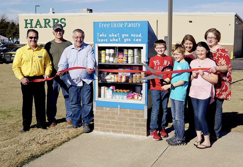 Westside Eagle Observer/RANDY MOLL Mayor Kevin Johnston, Paul Lemke of Springtown and Pastor Michael Powers look on as Gentry fourth-grade students Samuel Ernest, Samuel Jameson, Devyn Lemke and Reagan Rigney, accompanied by East facilitator and teacher Dorothy Ivey, cut the ribbon on a Free Little Panty located nextdoor to the Gentry Police Station on Thursday (Dec. 21. 2017). The mini food pantry was the idea of Gentry fourth-grade students and an East Initiative project to serve the needs of the community.