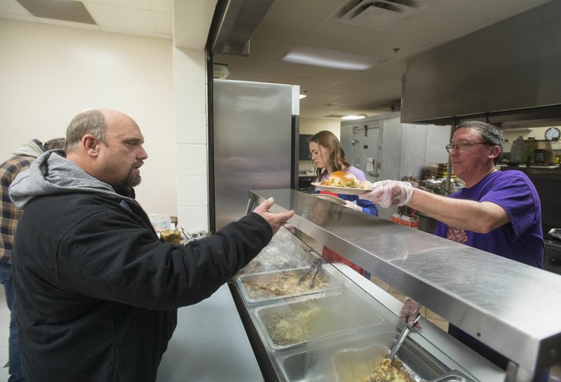 John Doyle (right) serves Michael Williams while serving the evening meal Tuesday at the Salvation Army Emergency Shelter in Bentonville. The Salvation Army of Northwest Arkansas has served roughly 70 to 80 meals per night this holiday season and kept its overnight shelters open for those seeking refuge from the cold.