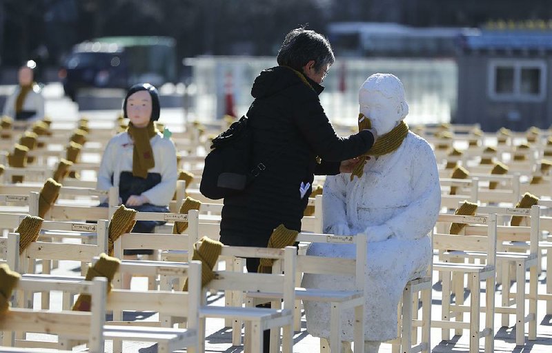 A woman adds a scarf to a statue representing a comfort woman at an installation Wednesday in Seoul, South Korea, symbolizing the Korean women who were forced into sexual slavery by Japanese occupiers during World War II.  