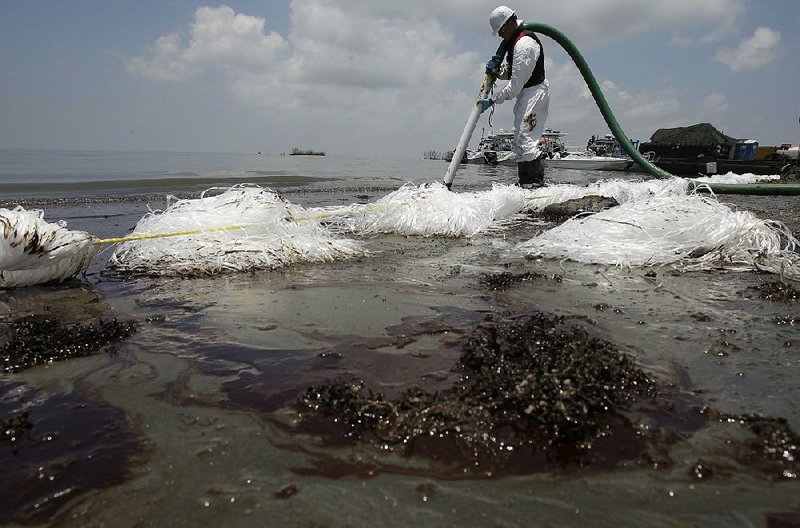 A worker uses a suction hose in June of 2010 to remove oil washed ashore from the Deepwater Horizon spill, off the coast of Louisiana.