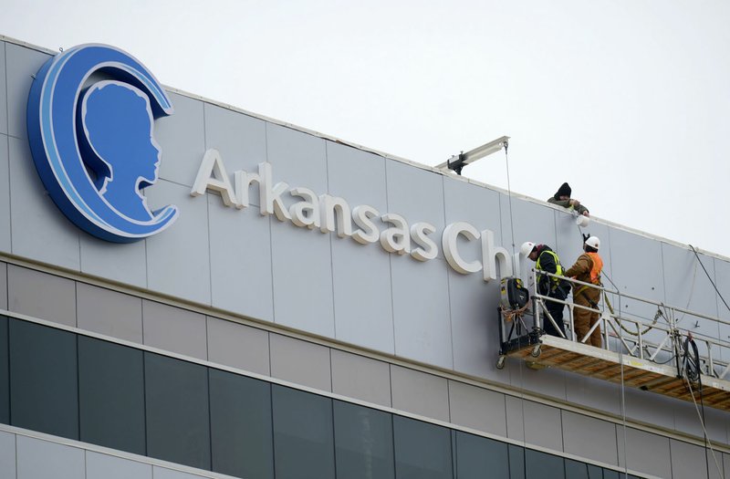 NWA Democrat-Gazette/ANDY SHUPE A worker passes the dot to the letter "I" to another worker Friday while assembling a sign from a gondola atop the nearly completed Arkansas Children's Northwest hospital in Springdale. The hospital is expected to open next month.