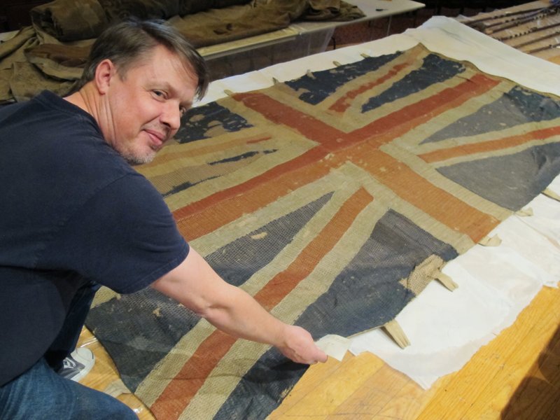 In this Thursday, Dec. 7, 2017, photo, Charles Swift, managing director and curator of the U.S. Naval Academy Museum in Annapolis, Md., looks up from a British flag of the HMS Landrail, which was captured in 1814 by American privateers sailing in the English Channel. It is one of 61 flags recently removed from glass cases at the U.S. Naval Academy for preservation. (AP Photo/Brian Witte)