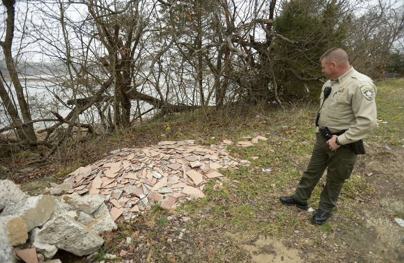 Cpl. Jason Nubbie of the Washington County Sheriff's Office, inspects a large pile of construction debris Friday, Dec. 22, 2017, that had been dumped near the shore of Beaver Lake along Blue Springs Road in Washington County. Nubbie helps to coordinate community service cleanups and planned to bring a crew of workers to the site at a later date. Washington and Benton counties field and investigate hundreds of calls per year about illegal dump sites, much of which are near rivers that feed into Beaver Lake.