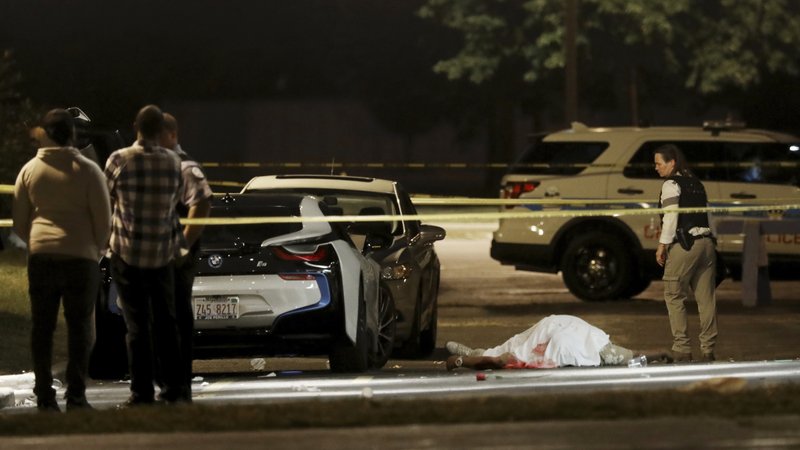 FILE - In this Aug. 20, 2017, file photo, a police detective walks past the body of a man fatally shot in the parking lot of an event center in Chicago. Several others were shot and transported to area hospitals. Chicago ended 2017 with fewer homicides than the year before but raging gang wars in the city's most violent neighborhoods drove the total beyond the 600 mark for just the second time in well over a decade. (John J. Kim/Chicago Tribune via AP, File)