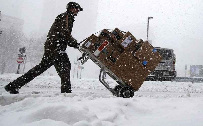 A deliveryman wheels packages across a snow-covered Boston street on Thursday. A foot of snow was forecast for the Boston area.