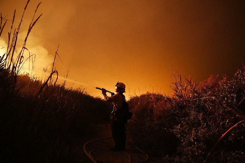 Firefighter Ryan Spencer battles a wildfi re along a hillside in La Conchita, Calif., last month. Wildfires along the West Coast helped raise the total bill for last year’s weather disasters to $306 billion in the United States.
